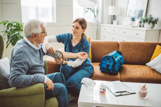 istockphoto-2003762957-612x612 Nurse visiting mature patient at home. She is measuring blood pressure to patient at his living room.